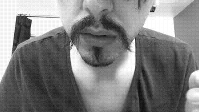 A Man With A Mustache And A Beard Is Wearing A Black Shirt In A Black And White Photo . GIF