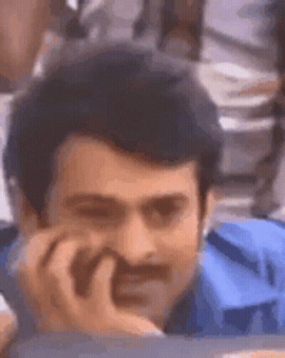 A Man With A Mustache And A Blue Shirt Is Sitting At A Table With His Hand On His Chin . GIF