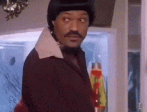 A Man With A Mustache And A Hat Is Standing In Front Of A Window . GIF