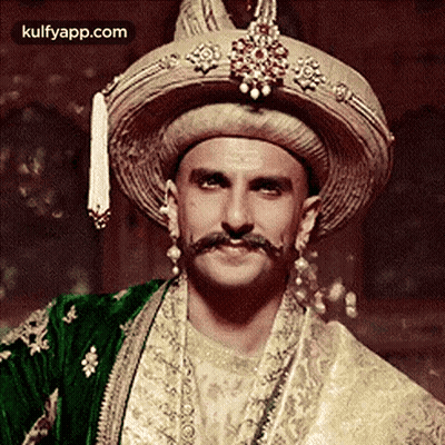 A Man With A Mustache And A Hat Is Wearing A Traditional Indian Outfit . GIF