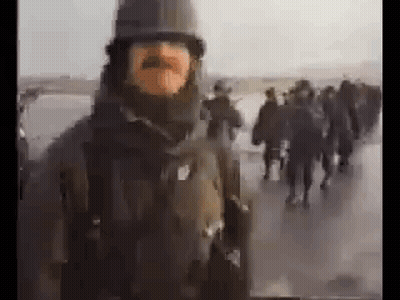 A Man With A Mustache And A Helmet Is Standing In Front Of A Group Of People . GIF