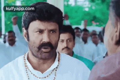 A Man With A Mustache And A Necklace Is Talking To Another Man In A Crowd Of People . GIF