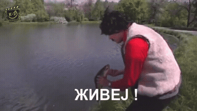 A Man With A Mustache And A Red Jacket Is Standing In Front Of A Tree And Says Живоj ! GIF