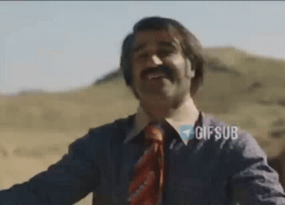 A Man With A Mustache And A Tie Is Smiling While Standing In The Desert . GIF