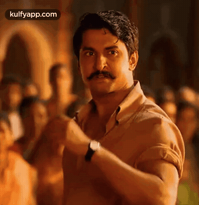 A Man With A Mustache And A Watch Is Standing In Front Of A Crowd Of People . GIF