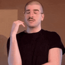 A Man With A Mustache And Glasses Is Wearing A Black Shirt And Making A Funny Face . GIF