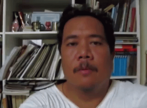 A Man With A Mustache In Front Of A Bookshelf Full Of Books GIF