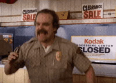 A Man With A Mustache Is Dancing In Front Of A Kodak Processing Center Closed Sign . GIF