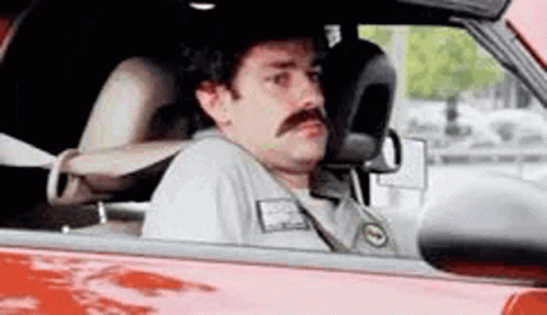 A Man With A Mustache Is Driving A Red Car And Looking Out The Window . GIF