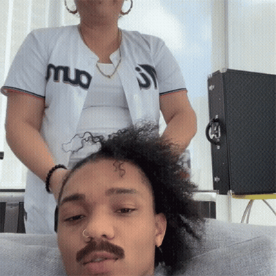 A Man With A Mustache Is Getting His Hair Done By A Woman Wearing A Jersey That Says Muo On It GIF