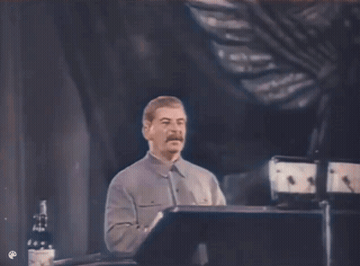 A Man With A Mustache Is Giving A Speech On A Stage GIF
