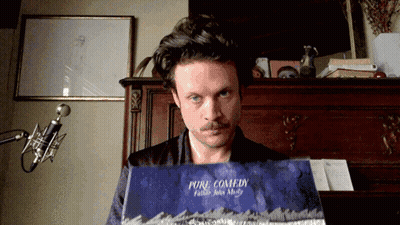 A Man With A Mustache Is Holding A Book Called Pure Comedy GIF