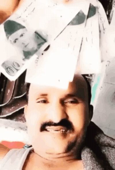 A Man With A Mustache Is Holding A Stack Of Money In Front Of His Face . GIF