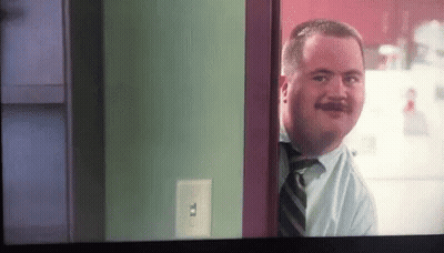 A Man With A Mustache Is Looking Through A Doorway GIF