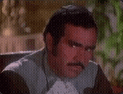 A Man With A Mustache Is Making A Funny Face While Sitting Down . GIF