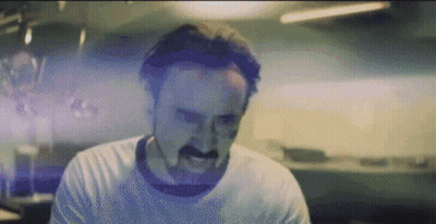 A Man With A Mustache Is Making A Funny Face While Wearing A White Shirt . GIF