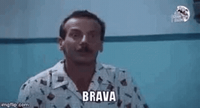 A Man With A Mustache Is Pointing At The Camera While Wearing A Shirt That Says Brava . GIF