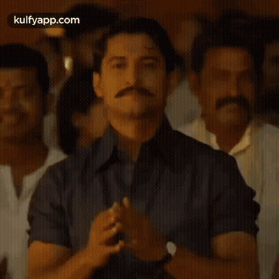 A Man With A Mustache Is Praying With His Hands Together In Front Of A Crowd Of People . GIF