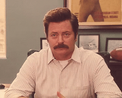 A Man With A Mustache Is Sitting At A Desk In Front Of A Framed Picture Of A Football Player .. GIF