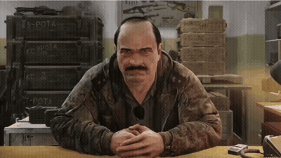 A Man With A Mustache Is Sitting At A Desk With His Hands Folded In Front Of A Stack Of Boxes . GIF