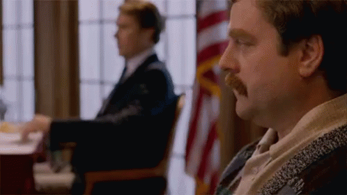 A Man With A Mustache Is Sitting At A Table In Front Of A Window . GIF