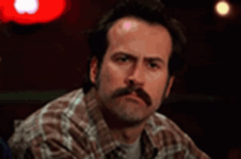 A Man With A Mustache Is Sitting At A Table Looking At The Camera . GIF