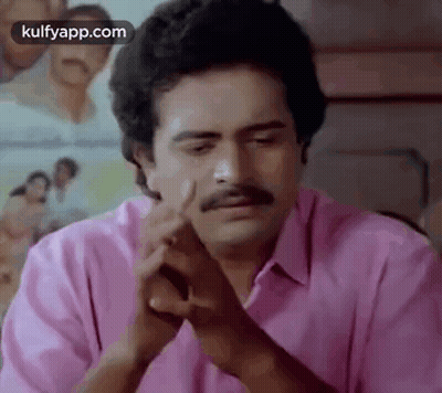 A Man With A Mustache Is Sitting At A Table With His Hands Folded In Front Of Him . GIF