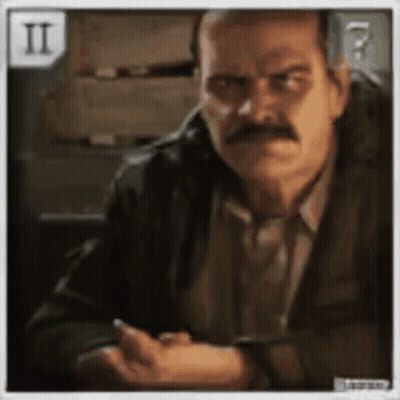 A Man With A Mustache Is Sitting At A Table With His Hands Folded GIF