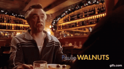 A Man With A Mustache Is Sitting At A Table With Paulie Walnuts In Yellow Letters GIF