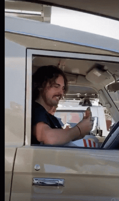 A Man With A Mustache Is Sitting In A Car Eating A Hamburger GIF