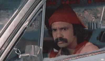A Man With A Mustache Is Sitting In A Car Wearing A Red Hat . GIF