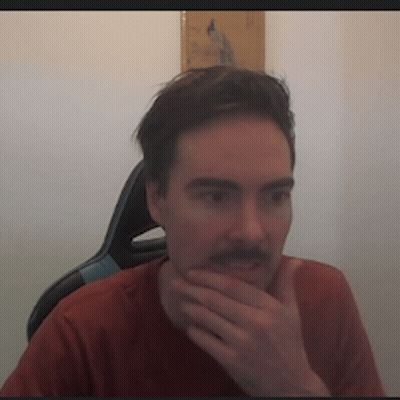 a man with a mustache is sitting in a chair with his hand on his chin .