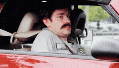 A Man With A Mustache Is Sitting In A Red Car Looking Out The Window . GIF
