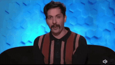 A Man With A Mustache Is Sitting In Front Of A Blue Wall GIF