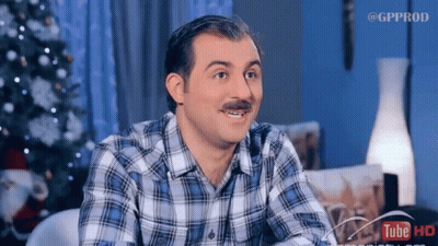 A Man With A Mustache Is Sitting In Front Of A Christmas Tree And A Sign That Says Tube Hd GIF