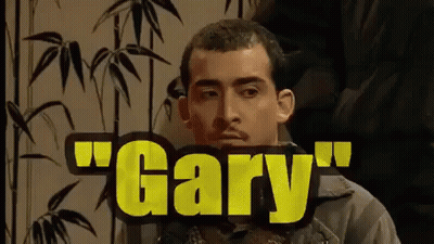 A Man With A Mustache Is Sitting In Front Of A Sign That Says Gary . GIF