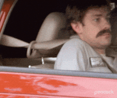 A Man With A Mustache Is Sitting In The Driver 'S Seat Of A Red Car On Peacock GIF