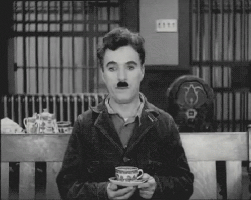 A Man With A Mustache Is Sitting On A Bench Holding A Cup Of Tea . GIF
