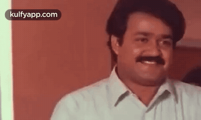 A Man With A Mustache Is Smiling And Looking At The Camera In A Room . GIF