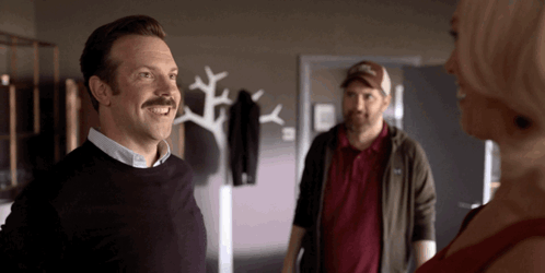 A Man With A Mustache Is Smiling In Front Of A Woman GIF
