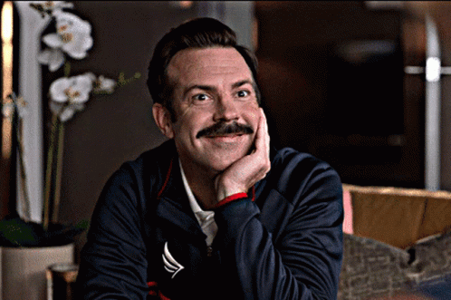 A Man With A Mustache Is Smiling With His Hand On His Chin While Wearing A Nautica Jacket GIF