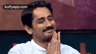 A Man With A Mustache Is Smiling With His Hands Folded In Front Of Him . GIF