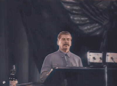 A Man With A Mustache Is Standing At A Podium Giving A Speech In A Dark Room . GIF