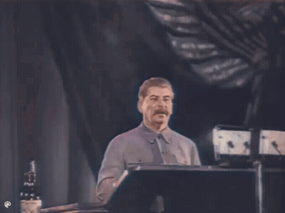 A Man With A Mustache Is Standing At A Podium Giving A Speech In A Dark Room . GIF