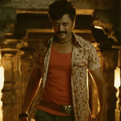 A Man With A Mustache Is Standing In A Dark Room With A Light Shining On Him GIF