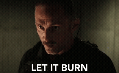 A Man With A Mustache Is Standing In A Dark Room With The Words `` Let It Burn '' Written On The Screen . GIF