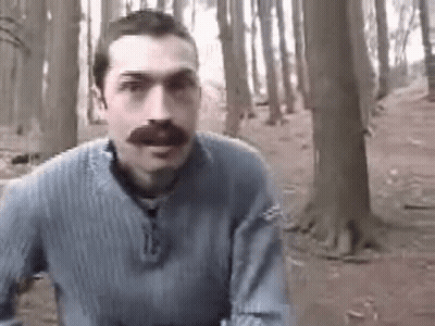 A Man With A Mustache Is Standing In A Forest . GIF