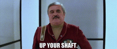 A Man With A Mustache Is Standing In A Hallway With The Words `` Up Your Shaft '' Written On The Screen . GIF