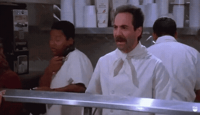 A Man With A Mustache Is Standing In A Kitchen Talking On A Phone . GIF