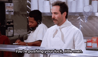 A Man With A Mustache Is Standing In Front Of A Counter In A Restaurant And Talking On A Phone . GIF